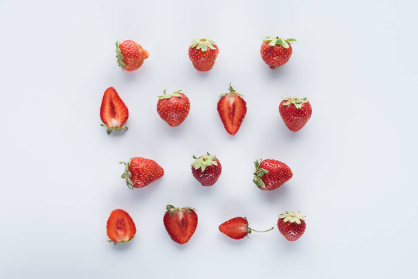 top view of halved and whole strawberries on white surface - Foto, immagini