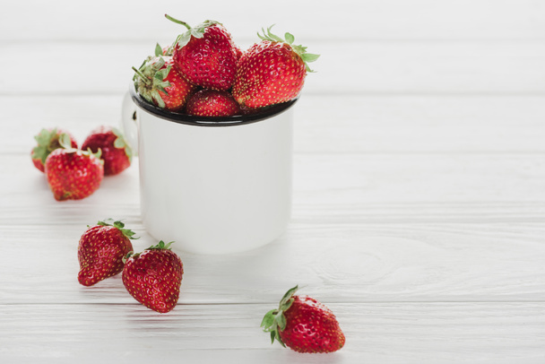 mug of ripe strawberries on white wooden tabletop - Fotó, kép