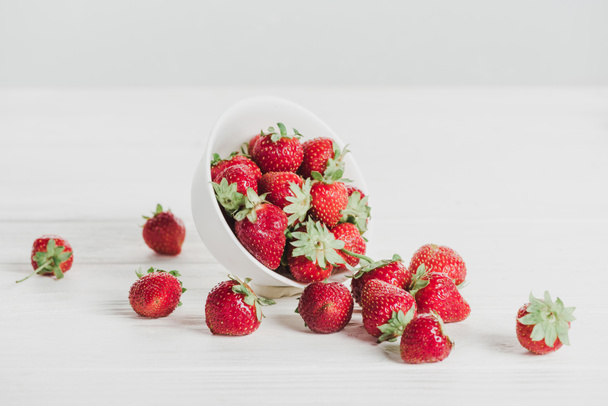Nahaufnahme von Erdbeeren verschüttet aus Schüssel auf weißer Oberfläche - Foto, Bild