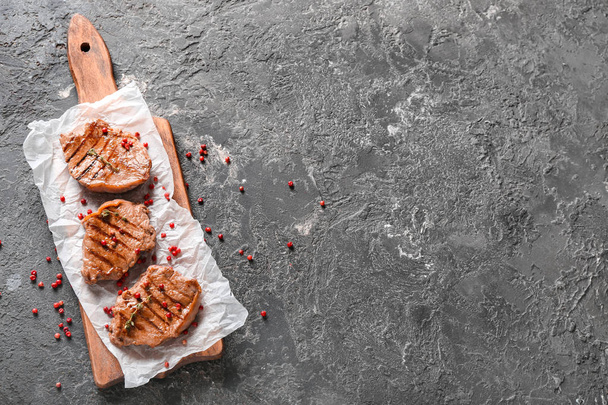 Puinen lauta herkullisia grillattuja pihvejä ja vaaleanpunainen pippuri harmaa pöytä
 - Valokuva, kuva