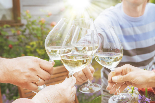Family of different ages people cheerfully celebrate outdoors with glasses of white wine, proclaim toast People having dinner in a home garden in summer sunlight. - Photo, Image
