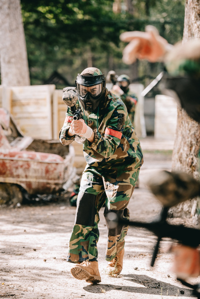 partial view of paintball player in uniform doing follow me gesture to his team outdoors - Foto, afbeelding
