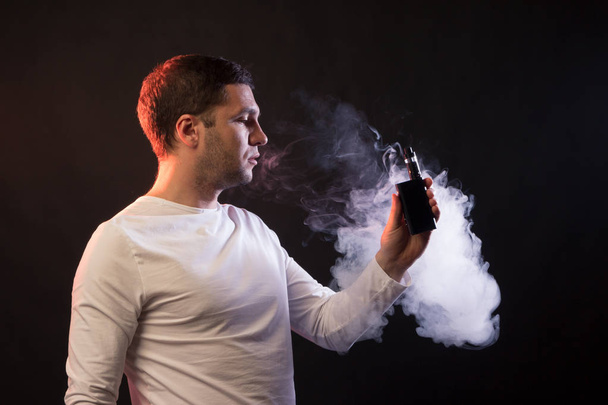 El hombre está fumando vapor. Retrato en estudio sobre fondo negro. Concepto de dependencia del tabaco
 - Foto, imagen