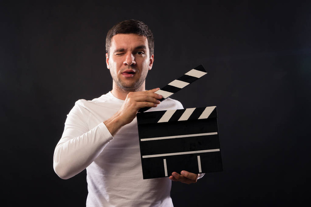 Jongeman van blanke verschijning houdt een Filmklapper. Portret in de studio op een zwarte achtergrond met rook en rode en blauwe studio licht geschoten.  - Foto, afbeelding