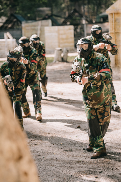 paintball team in uniform and protective masks playing paintball with marker guns outdoors - Photo, Image