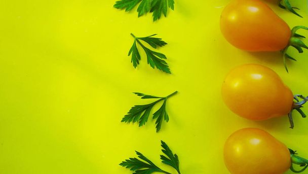 小さな黄色のトマト、黄色の背景にパセリ. - 写真・画像