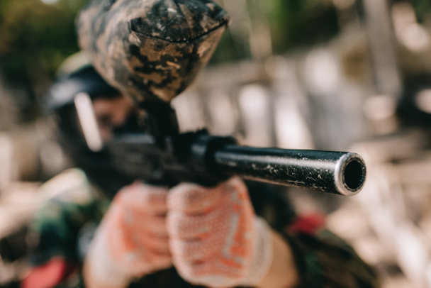 selective focus of paintball player in camouflage aiming by paintball gun outdoors  - Fotografie, Obrázek
