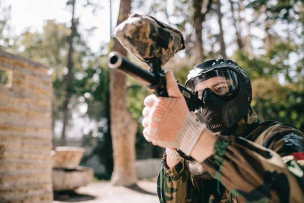 concentrated male paintball player in goggle mask and camouflage aiming by paintball gun outdoors  - Fotografie, Obrázek