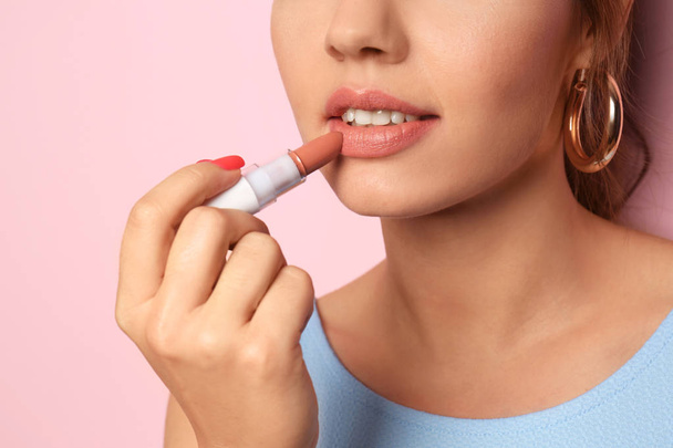 Beautiful young woman applying pink lipstick on color background, closeup - Fotó, kép