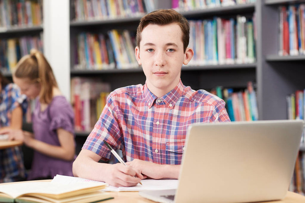 Porträt eines männlichen Gymnasiasten, der in der Bibliothek am Laptop arbeitet - Foto, Bild