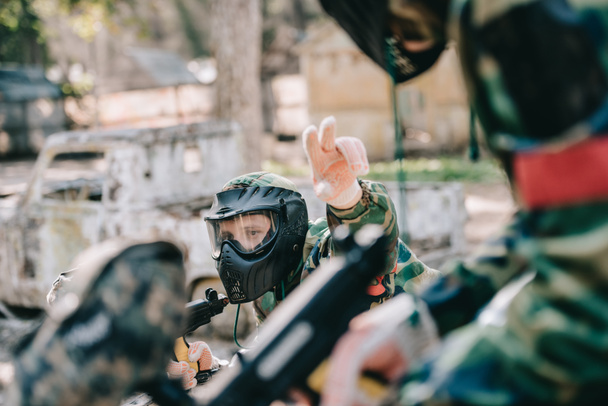 male paintball player in camouflage with marker gun uniform pointing by fingers to his team outdoors - Photo, Image