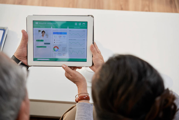 Вид ззаду старшої пари, що використовує програму моніторингу здоров'я на цифровому планшеті
  - Фото, зображення