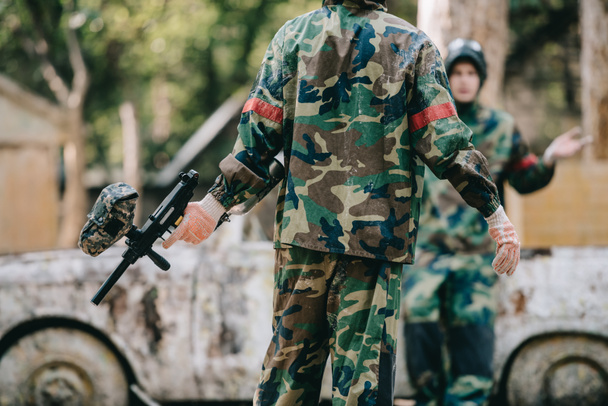 partial view of paintball players in camouflage uniform resting near broken car outdoors  - Photo, Image