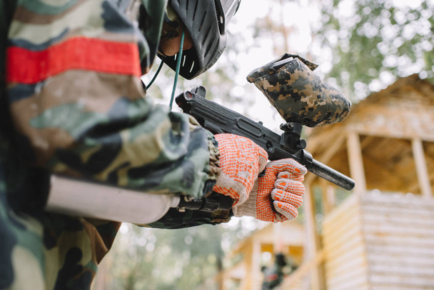 partial view of male paintball player in goggle mask and camouflage with paintball gun outdoors  - Fotografie, Obrázek