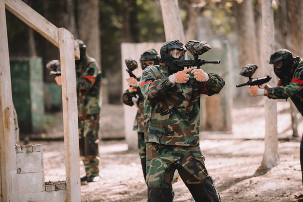 paintball team in uniform and protective masks shooting by paintball guns outdoors - Foto, Imagen