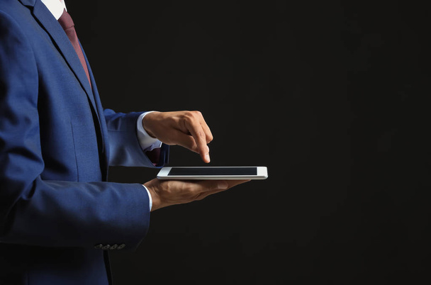 Businessman with tablet PC on dark background - Valokuva, kuva