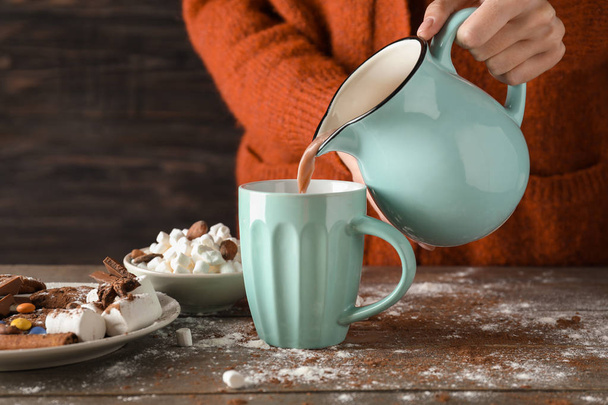 Woman pouring tasty cocoa from jug into cup on wooden table - Photo, Image