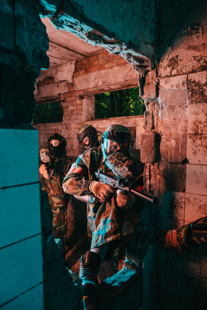 paintball team in uniform and protective masks playing paintball with marker guns in abandoned building - Fotografie, Obrázek