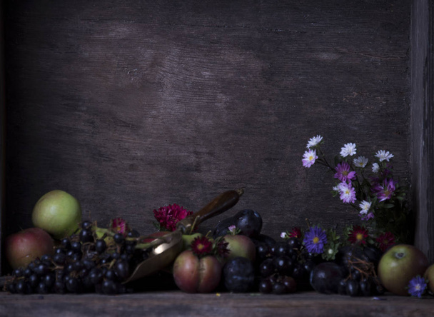Apples, plums, grapes and flowers on dark grey shabby background - Фото, изображение