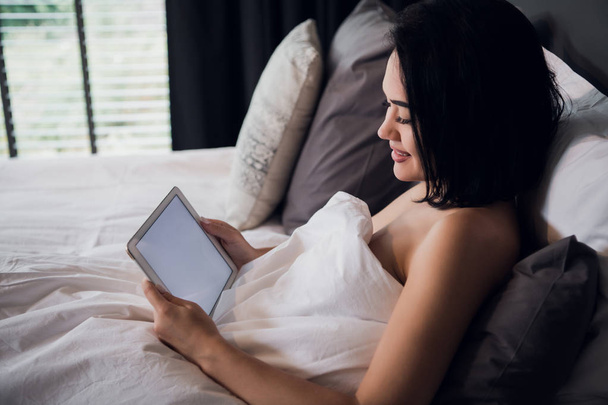 attractive brunette girl holding digital tablet with blank screen and smiling in bedroom - Fotoğraf, Görsel