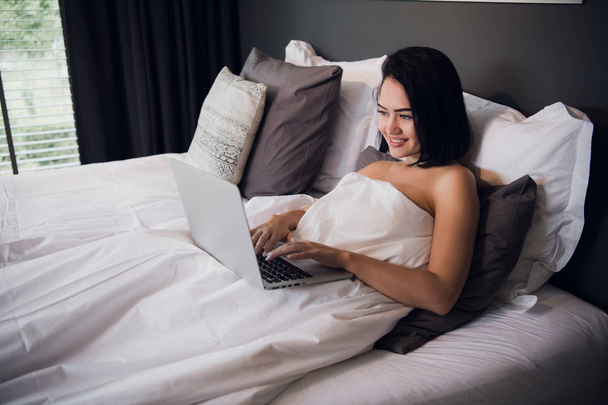 Porträt einer schönen jungen Frau mit Laptop auf dem Bett - Foto, Bild