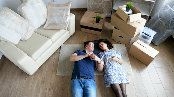 Κορυφαία θέα ζευγάρι ξαπλωμένο στο πάτωμα του νέου σπιτιού - Πλάνα, βίντεο