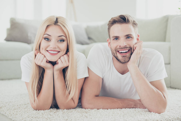 Close-up portrait of beautiful attractive lovely nice cute cheerful adorable dreamy couple in white t-shirts at home, lying on carpet, light interior - Photo, Image