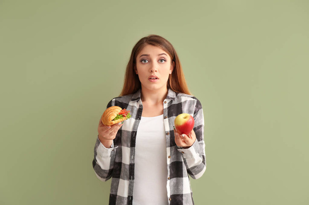 junge Frau wählt zwischen Croissant und Apfel auf farbigem Hintergrund - Foto, Bild