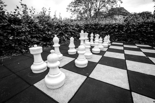 Παιχνίδι σκάκι με μεγάλα κομμάτια σε έναν υπαίθριο κήπο σε monchrome χρώματα - Φωτογραφία, εικόνα