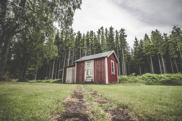 Rote Hütte in einem schwedischen Wald mit Kiefern mit Warnplanken und verwitterter Farbe - Foto, Bild
