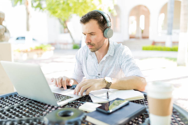Homem de negócios adulto médio focado usando fones de ouvido enquanto trabalhava em laptop no jardim
 - Foto, Imagem