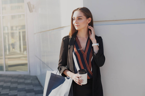 Young attractive woman exits from shopping mall with glass of coffee and package. Sale and business concept - Fotoğraf, Görsel