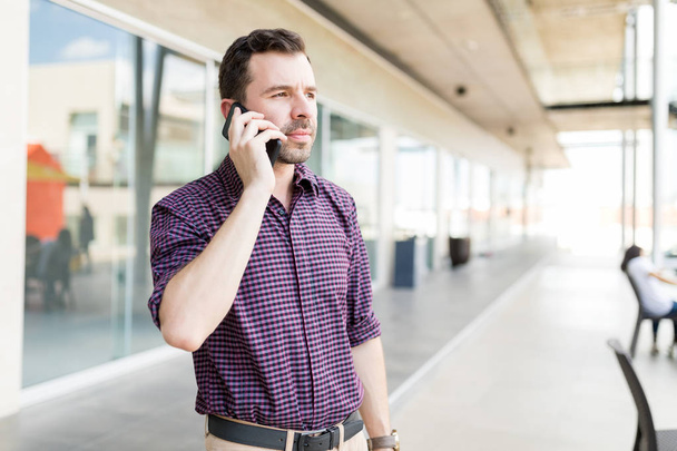 Взрослый мужчина отвечает на звонки со смартфона, стоя в торговом центре
 - Фото, изображение