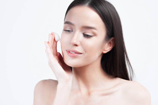 Young beautiful woman applies cream on clean perfect skin. Skin care and age cosmetics concept - 写真・画像