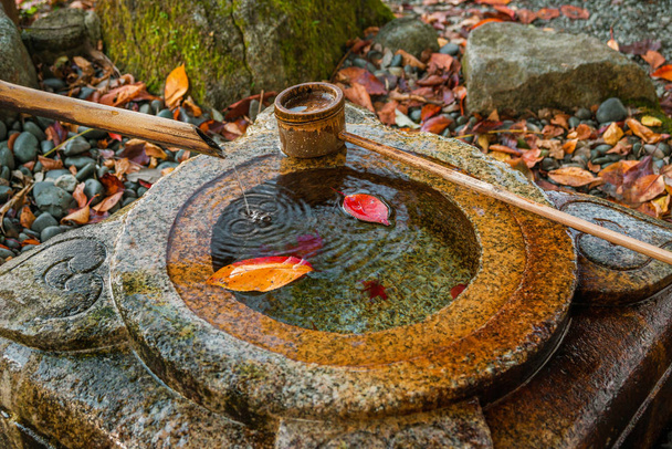 Vanha kivi chozubachi rituaalinen puhdistautuminen Japanissa, bambu kauha ja syksyn punainen ja keltainen lehdet sisällä
 - Valokuva, kuva
