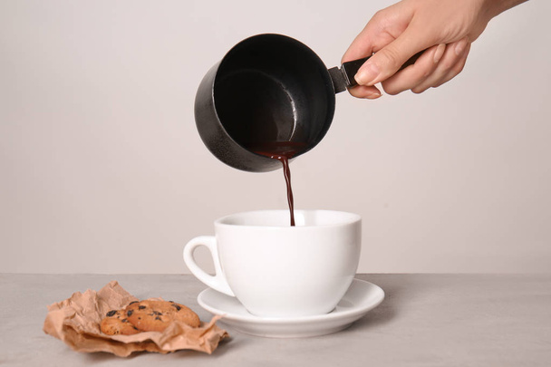 Woman pouring hot chocolate from cezve into cup on light table - Foto, afbeelding