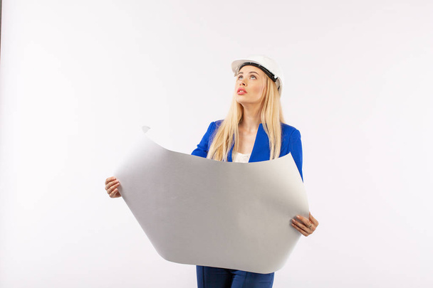 Mulher empregada de terno em pé no capacete com documentos em papel sobre fundo branco. arquiteto considera desenhos
 - Foto, Imagem