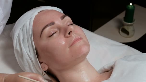 Επαγγελματίας αισθητικός εφαρμογή καλλυντικών μάσκα στο γυναικείο λαιμό στο σαλόνι ομορφιάς. Η διαδικασία για την εφαρμογή ενός διαφανούς gel με πινέλο στο πρόσωπο τον πελάτη στο κέντρο κοσμετολογίας. - Πλάνα, βίντεο