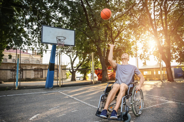 Νεαρός άνδρας σε αναπηρικό καροτσάκι να παίζει μπάσκετ σε εξωτερικούς χώρους - Φωτογραφία, εικόνα
