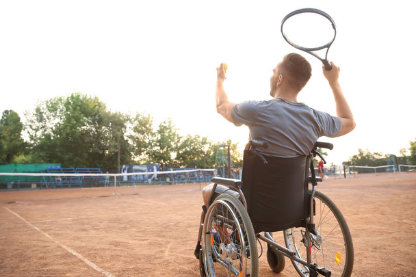 Молодой человек в инвалидной коляске играет в теннис на корте - Фото, изображение