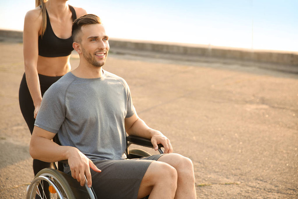 Sportowy kobieta pomaga młody człowiek na wózku inwalidzkim na zewnątrz - Zdjęcie, obraz