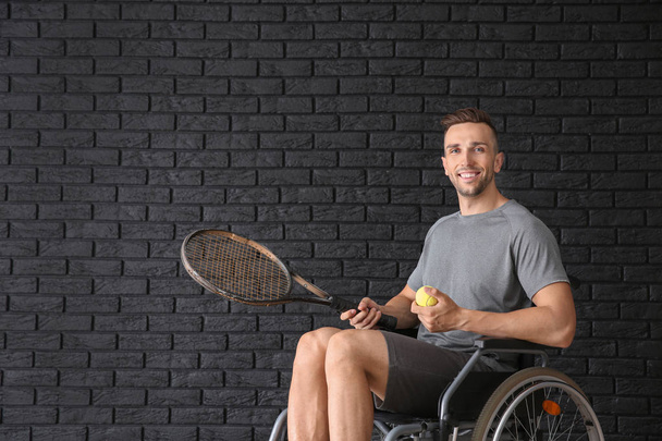 Νεαρός τενίστας που κάθεται σε αναπηρικό καροτσάκι, σκούρο τούβλο τοίχο - Φωτογραφία, εικόνα