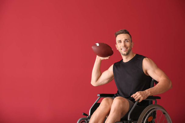 Giovane uomo con palla da rugby seduto in sedia a rotelle su sfondo colore
 - Foto, immagini