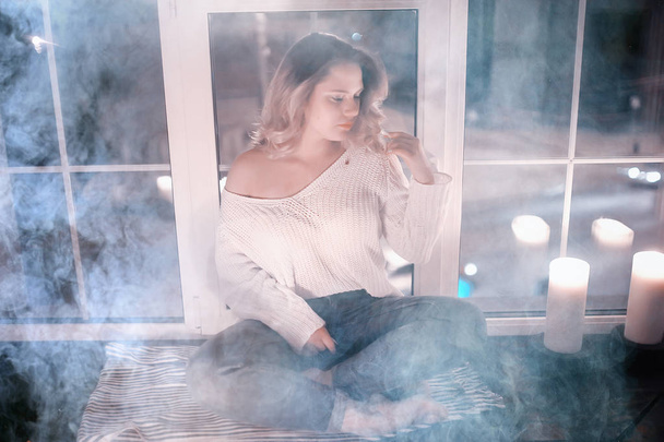 young blonde woman in white knitted sweater posing in dark room with smoke - Zdjęcie, obraz