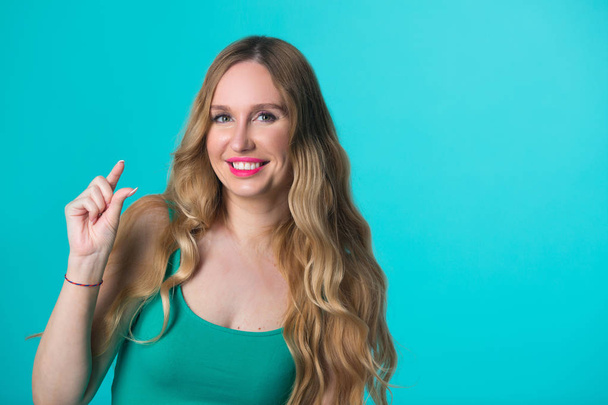 beautiful young girl with her hair on blue background with hand gesture - Foto, Imagem