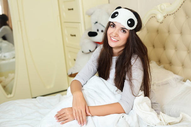 Joven mujer sonriente está sentada en una cama en la mañana
 - Foto, Imagen