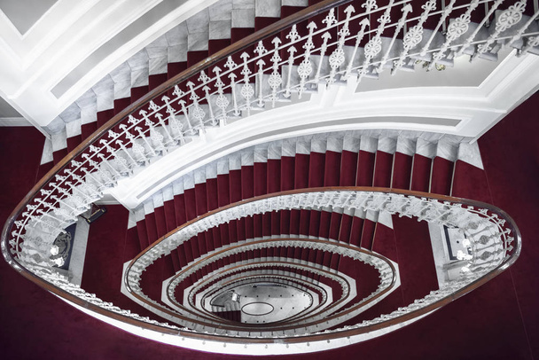 Simetría arquitectónica con elegantes escaleras de caracol, sobre la vista, hechas de mármol blanco y cubiertas con alfombra roja, en un hotel en Génova, Italia
. - Foto, imagen
