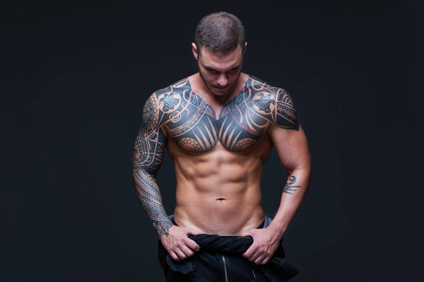 The man with a muscular naked torso with tattoos on the dark background. ABS. - 写真・画像