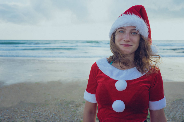 Girl dressed as Santa Claus standing on the beach or ocean. The concept of the journey to Christmas. Happy New Year and merry Christmas! - Фото, зображення