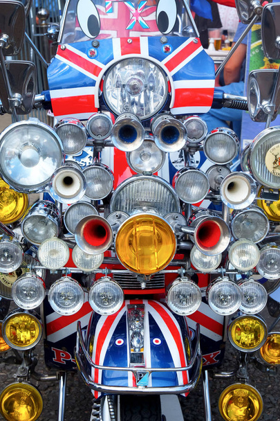 front view of a moped scooter that is painted in British union jack flag colors there are 20 head lights and four horns on the front of the moped - Photo, Image
